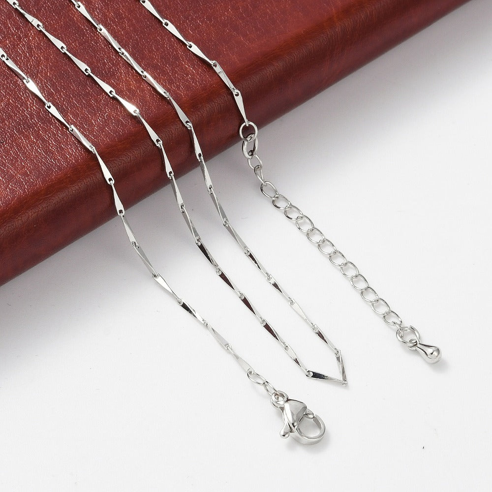 silver tone twisted bar link necklace with lobster claw clasp and extender chain draped over brown leather pad onto white surface.
