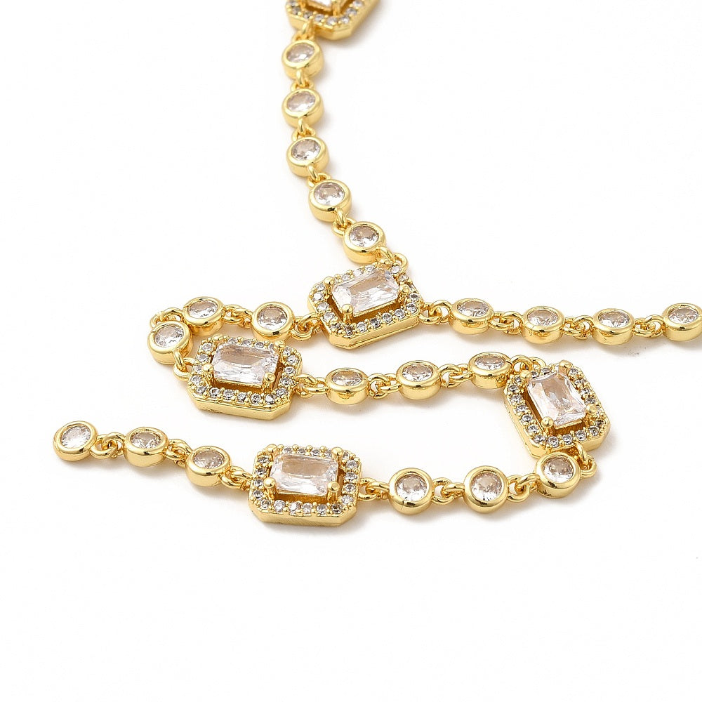 zoomed in front section of golden clear rectangle and round stone link lariat Y necklace over white surface. 