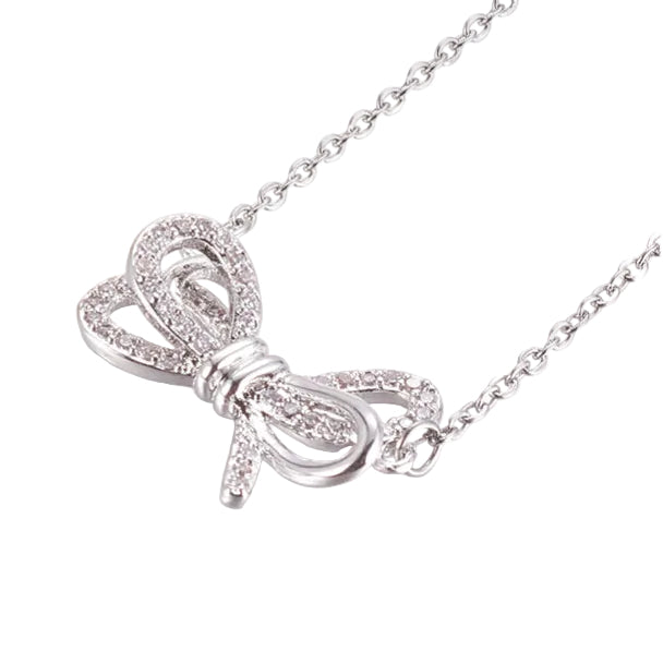 zoomed in front of silver tone bow pendant necklace with clear round stones on a cable chain over white background. 