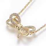 zoomed in front of golden bow pendant necklace with clear round stones on a cable chain over white background. 