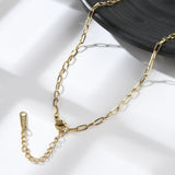 golden paperclip chain necklace with lobster claw clasp and extender chain draped over black plate edge onto white surface. 