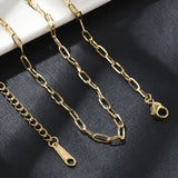 zoomed in sections of golden paperclip chain necklace with lobster claw clasp and extender chain draped over cream ledge onto black textured surface. 