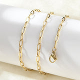 golden paperclip chain necklace with lobster claw clasp wrapped around white cylinder form on white surface. 