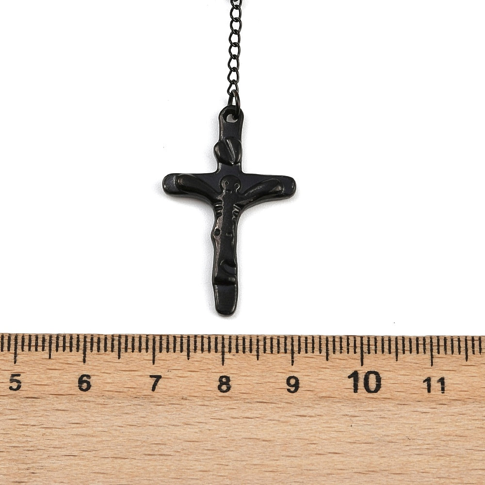 black crucifix from rosary bead necklace displayed over wooden ruler and white background. 