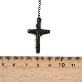 black crucifix from rosary bead necklace displayed over wooden ruler and white background. 