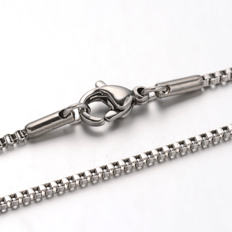 zoomed in sections of silver tone box chain necklace with lobster claw clasp over white background. 