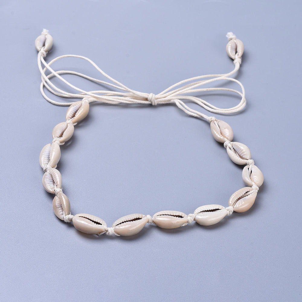 adjustable cowrie choker on white cord over light grey surface. 