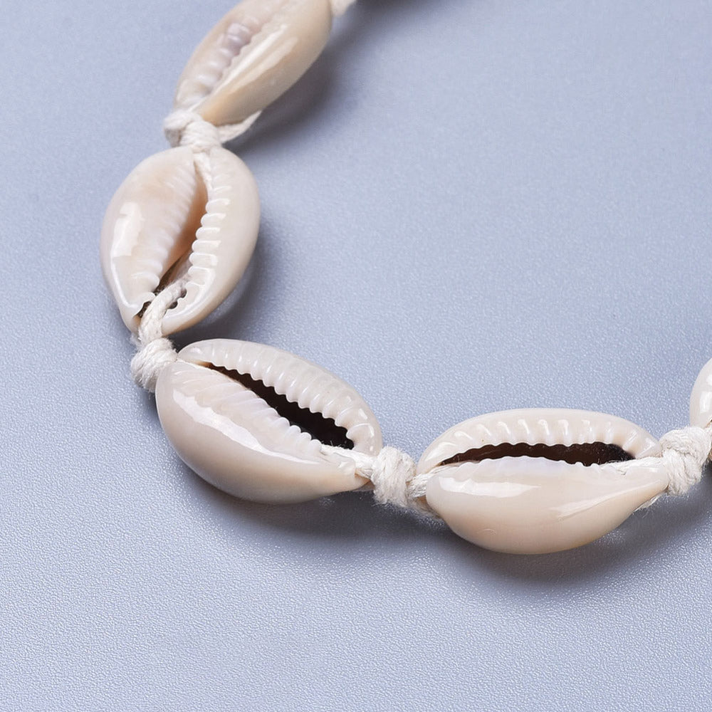 close-up of front of adjustable cowrie choker on white cord over light grey surface. 