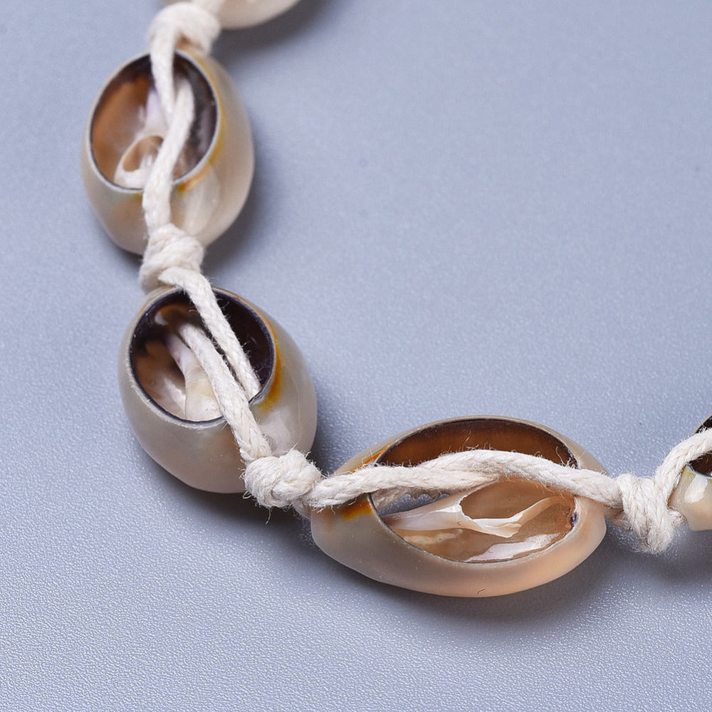 close-up of back of adjustable cowrie choker on white cord over light grey surface. 