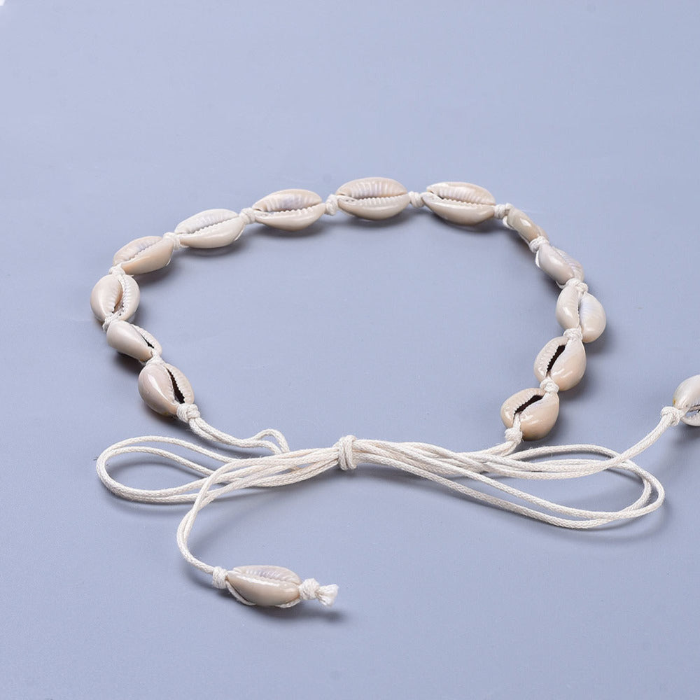 adjustable cowrie choker on white cord over light grey surface. 