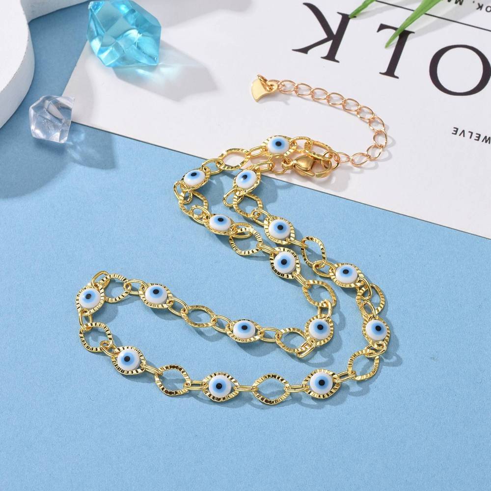 golden horse eye and evil eye link choker necklace with lobster claw clasp and extender chain over a white and light blue surface with clear and blue gem replicas in the corner. 