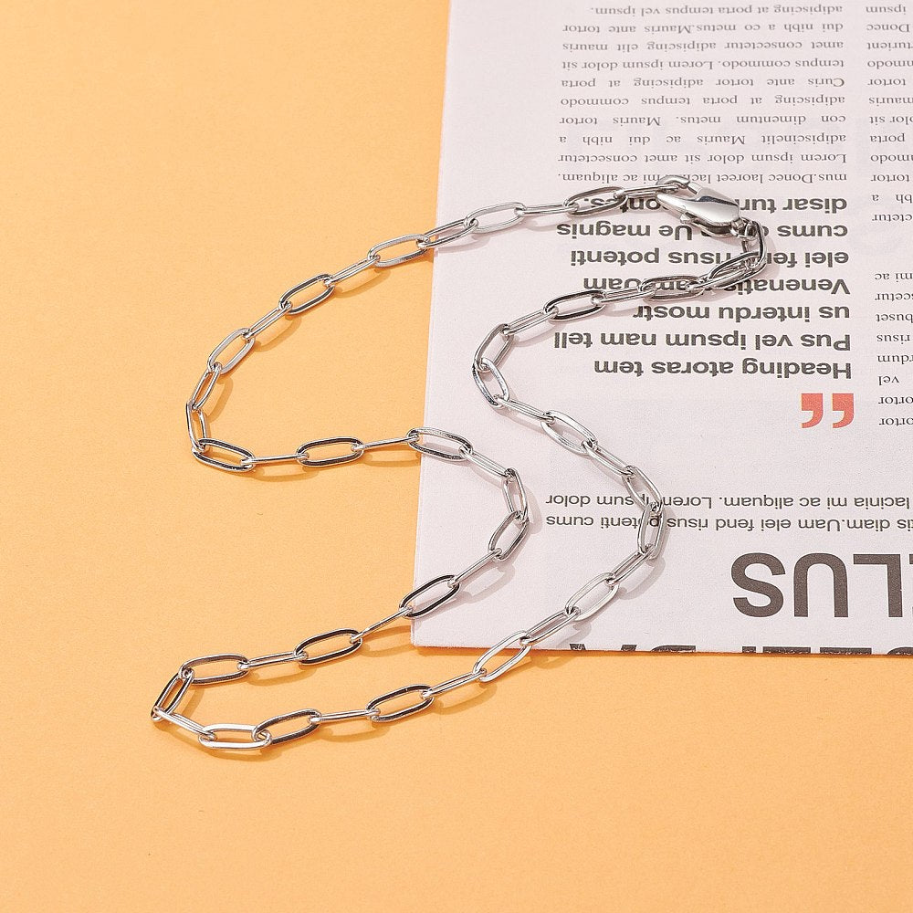 silver tone paperclip chain necklace with lobster claw over magazine article clipping over orange surface. 