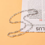 silver tone paperclip chain necklace with lobster claw over magazine article clipping over orange surface. 
