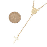zoomed in section of golden satellite chain rosary style necklace with Virgin Mary connector and cross pendant next to dollar coin over white background. 