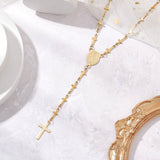 golden rosary style necklace featuring a traditional Virgin Mary connector and cross pendant while the links are made up of small crosses over a white background with the edge of an ornate gold frame plus white and gold tulle. 