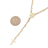 golden rosary style necklace featuring a traditional Virgin Mary connector and cross pendant while the links are made up of small crosses next to a dollar coin over a white background. 