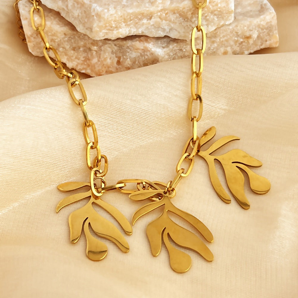 golden paperclip chain necklace with three leaf design drops draped over stone slabs onto a cream cloth surface. 