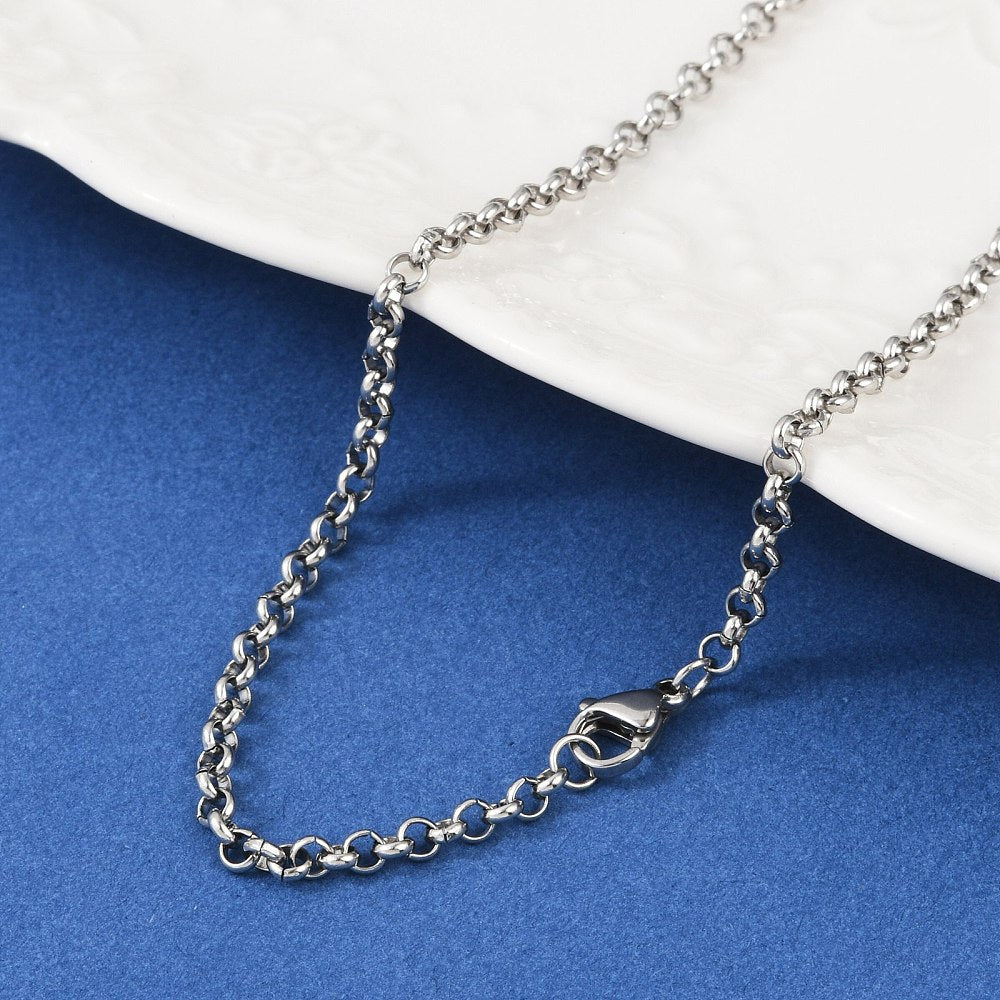 silver tone Rolo chain necklace with lobster claw clasp draped over white dish onto blue felt surface. 