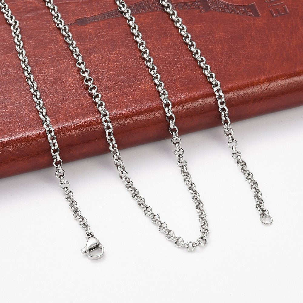 silver tone Rolo chain necklace with lobster claw clasp draped over leather book spine onto white surface. 