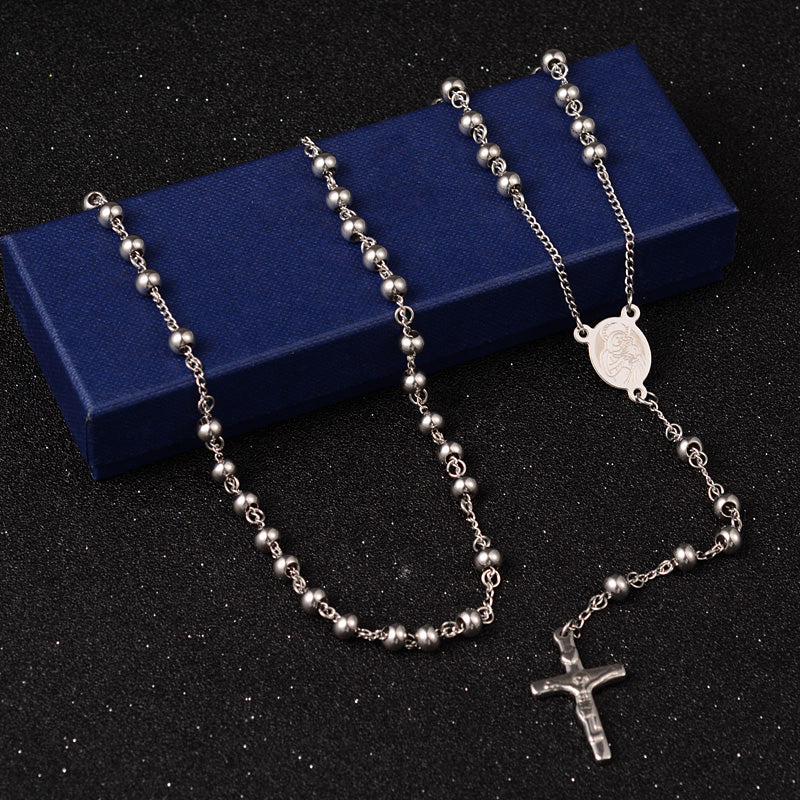 silver tone large bead rosary necklace with oval medal connector and crucifix pendant draped over blue box on black surface. 