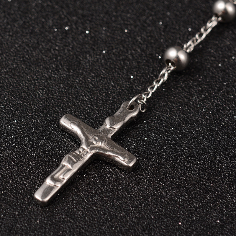 zoomed in front of silver tone crucifix pendant on rosary necklace over black surface. 