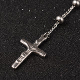 zoomed in front of silver tone crucifix pendant on rosary necklace over black surface. 