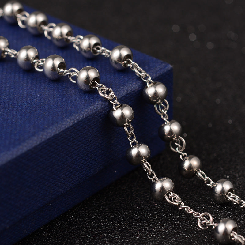 zoomed in section of large silver tone rosary bead necklace draped over blue box onto black surface. 