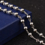 zoomed in section of large silver tone rosary bead necklace draped over blue box onto black surface. 