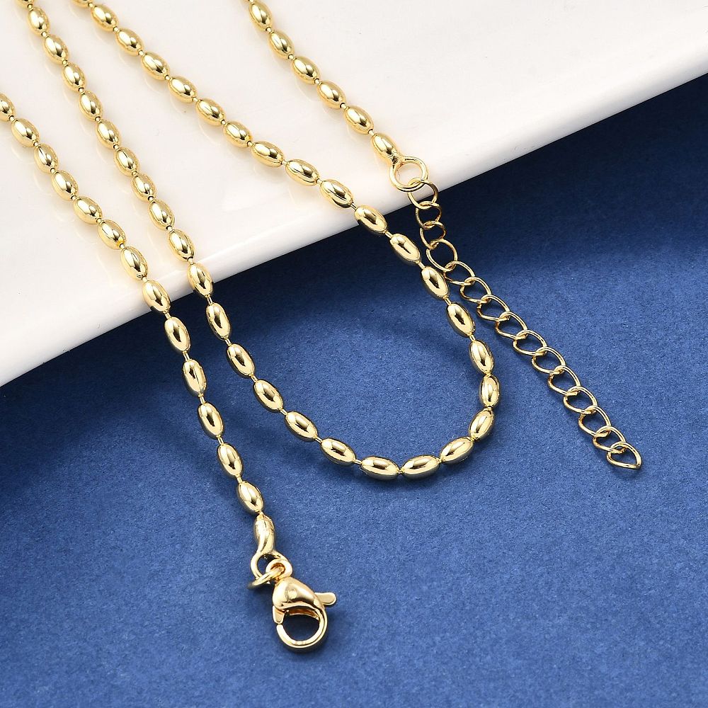 golden oval ball chain necklace with lobster claw clasp and extender chain draped over white ledge onto blue felt surface. 