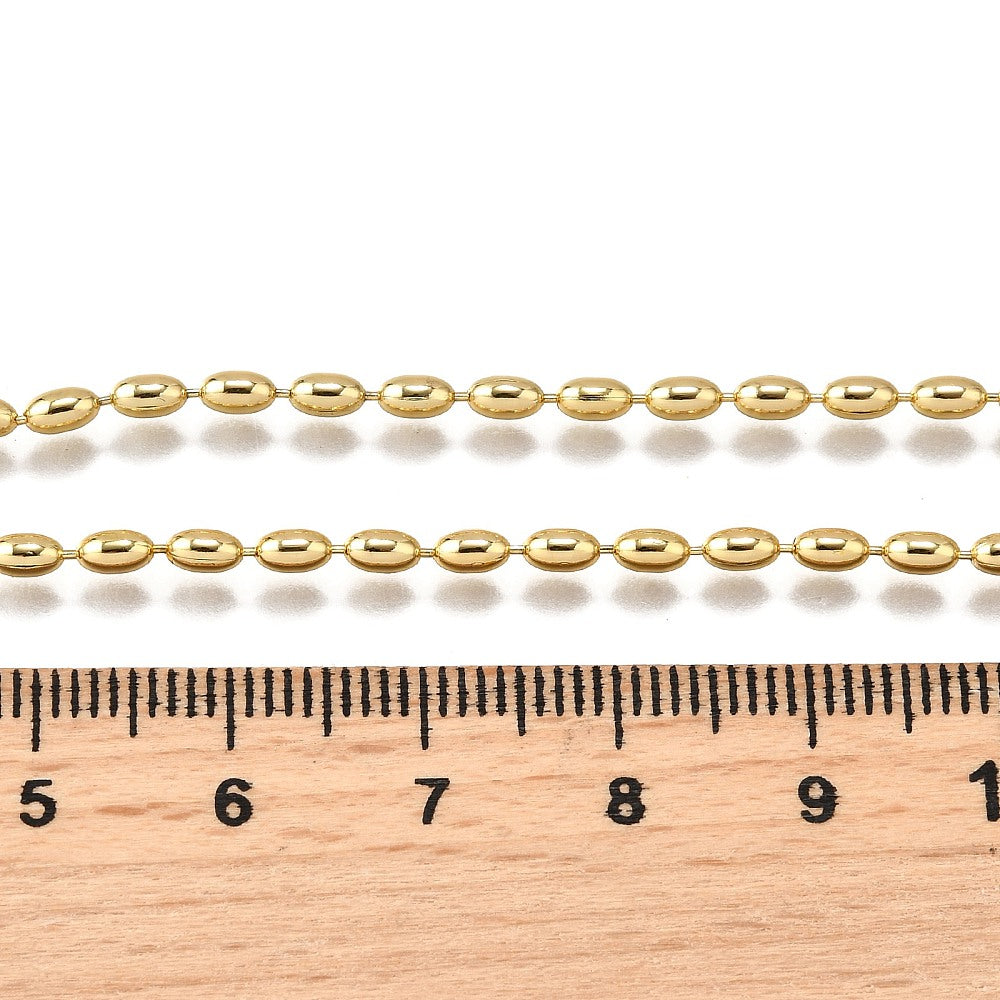 zoomed in section of golden oval ball chain necklace displayed above wooden ruler over white background. 