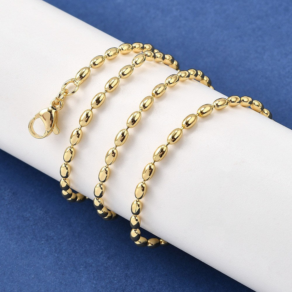 golden oval ball chain necklace with lobster claw clasp wrapped around white cylinder form over blue felt surface.  