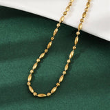 golden oval and round link ball chain necklace draped over white ledge onto green felt surface. 