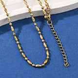 zoomed in sections of golden oval and round link ball chain necklace with lobster claw clasp and extender chain draped over white stone ledge onto blue felt surface. 