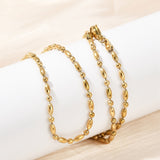 golden oval and round link ball chain necklace with lobster claw clasp wrapped around white cylinder form over light peach surface. 