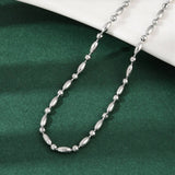 silver tone oval and round link ball chain necklace draped over white ledge onto green felt surface. 
