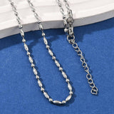 zoomed in sections of silver tone oval and round link ball chain necklace with lobster claw clasp and extender chain draped over white stone ledge onto blue felt surface. 