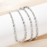 silver tone oval and round link ball chain necklace with lobster claw clasp wrapped around white cylinder form over light peach surface. 