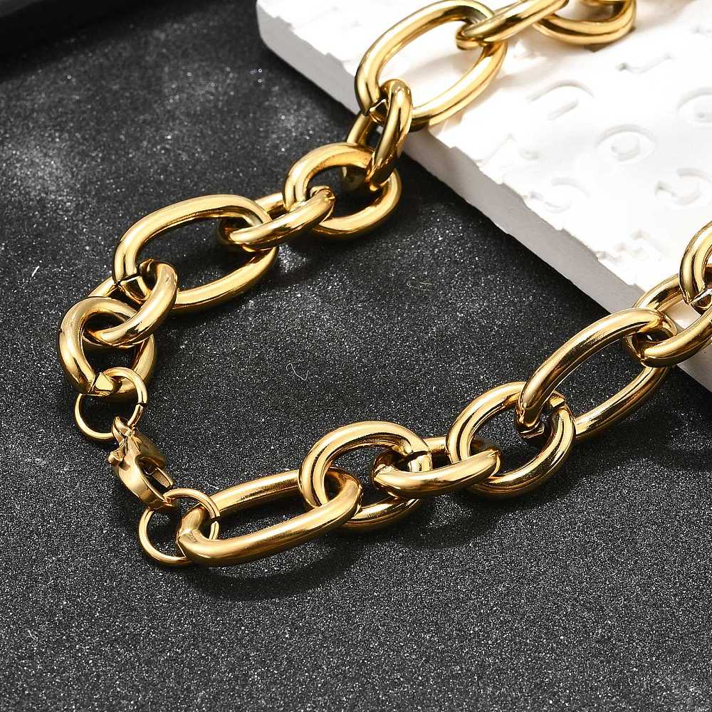 zoomed in section of golden, large alternating oval and round link chain necklace with lobster claw clasp draped over white tile onto textured black background. 