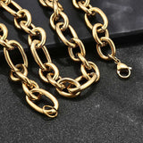 zoomed in sections of golden, large alternating oval and round link chain necklace with lobster claw clasp draped over black ledge onto textured black background. 