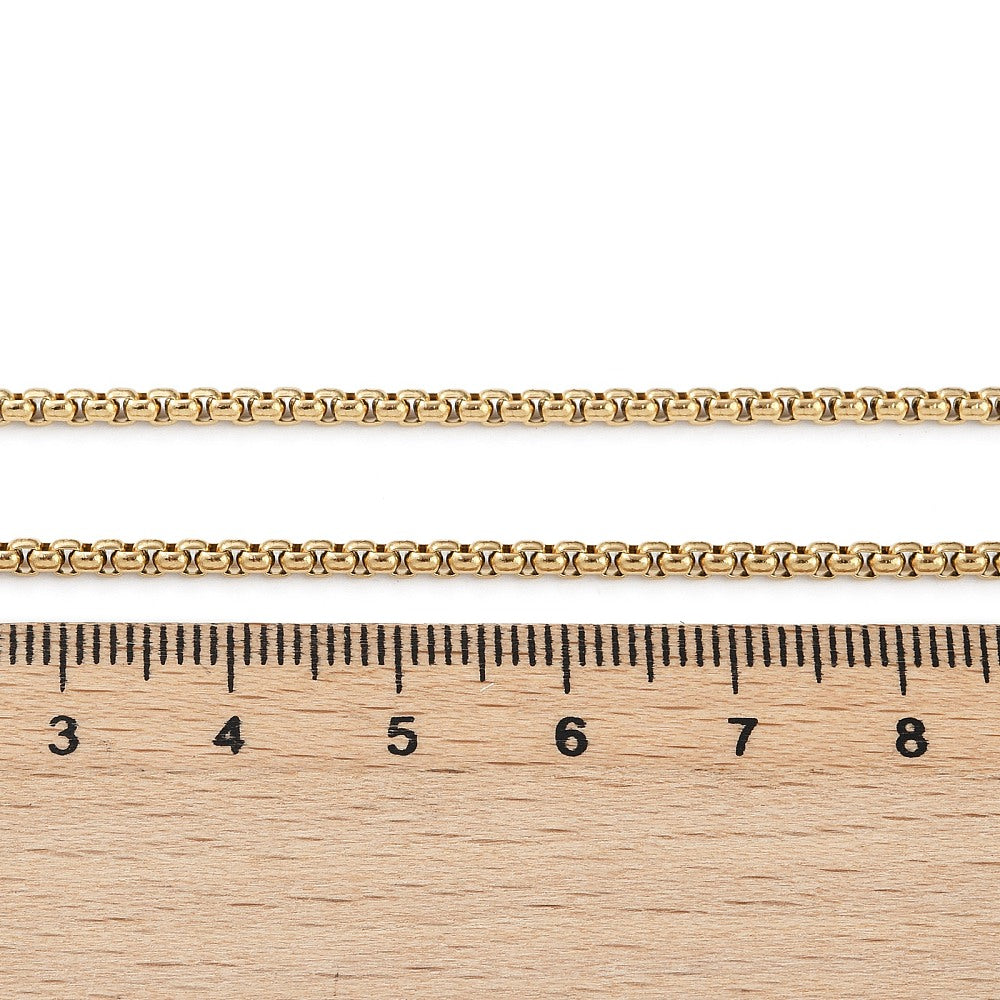 golden Venetian box chain displayed above wooden ruler on white background. 