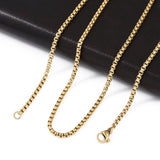 golden Venetian box chain with lobster claw clasp draped over a black leather folder onto a white surface. 
