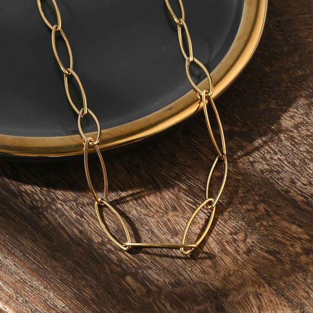 golden marquise paperclip chain draped over gold rimmed black plate onto wood grain surface.