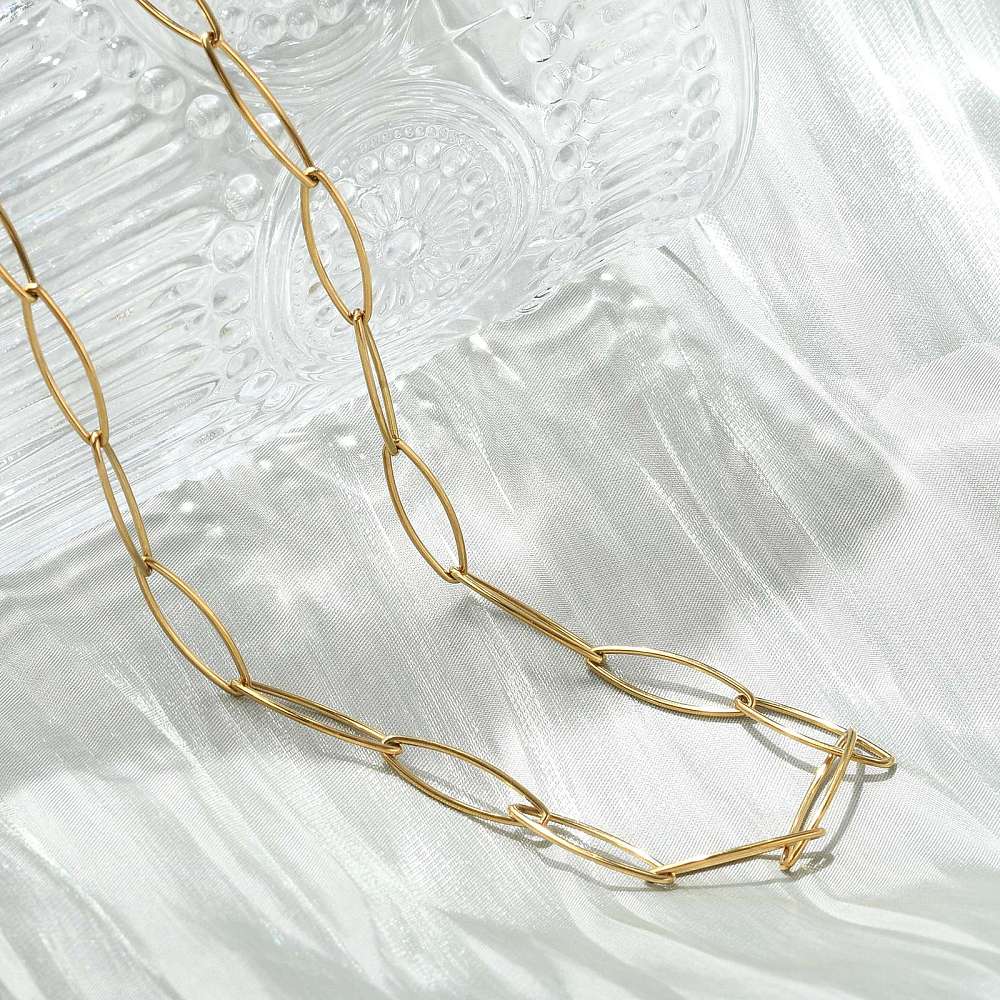 golden marquise paperclip chain necklace with lobster claw clasp and extender chain draped over crystal vase on white tablecloth. 