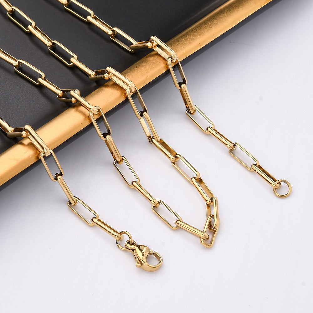 golden square paperclip chain draped over black and gold rimmed tray onto white surface. 