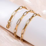 golden square paperclip necklace with lobster claw clasp wrapped around white cylinder form over a peach fabric surface. 