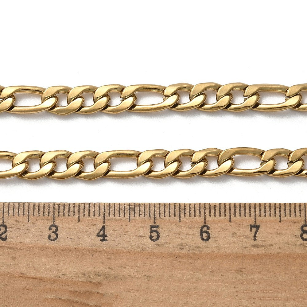 golden Figaro chain necklace with lobster claw clasp displayed above a wooden ruler on a white background. 