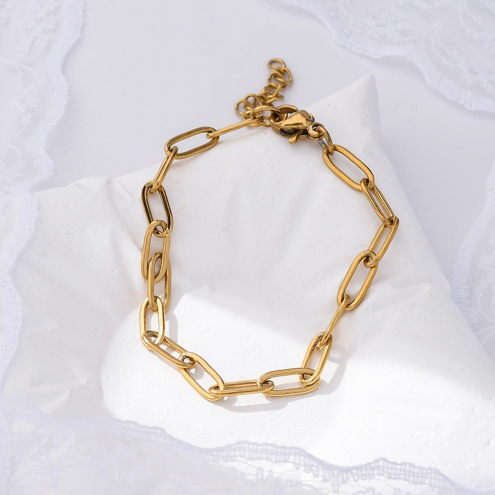 golden paperclip chain bracelet with lobster claw clasp and extender chain on white pillow over lacey white background. 