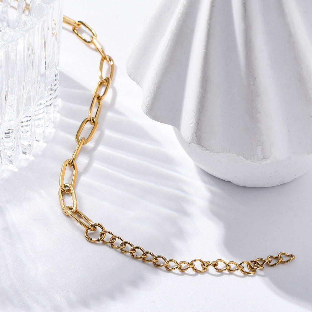 golden paperclip chain bracelet with lobster claw clasp and extender chain woven between a cut crystal bowl and white ceramic statue on a white surface. 