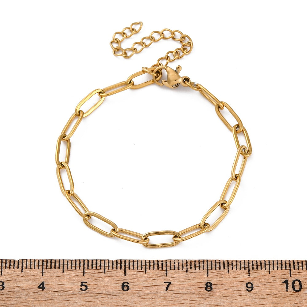 golden paperclip chain bracelet with lobster claw clasp and extender chain above wooden ruler over white background. 