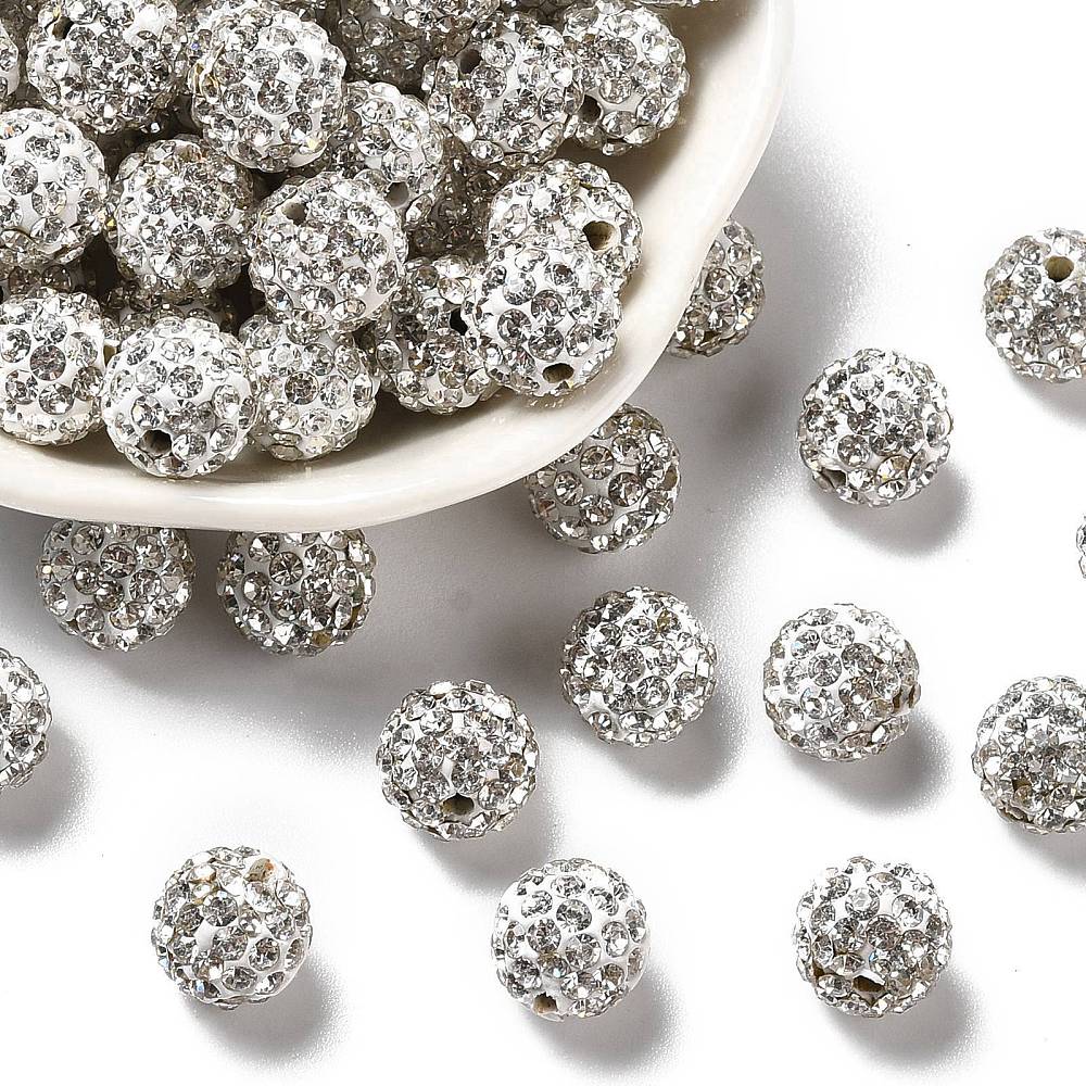 loose pave clear rhinestone clay beads in white bowl and some have spilled onto over white surface. 
